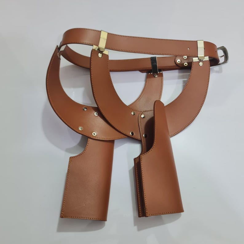 Puede incluir: Un arn&eacute;s de doble funda de cuero color canela que cuenta con un cintur&oacute;n con hebilla de metal, dos fundas verticales y remaches de metal dorado que conectan las correas estructurales. El dise&ntilde;o incluye componentes ajustables y una disposici&oacute;n sim&eacute;trica.