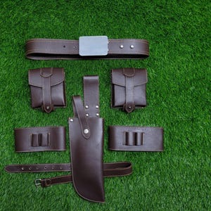 May include: A brown leather belt with a silver buckle, two small brown leather pouches, two brown leather straps with metal buckles, and a large brown leather sheath with a metal tip.