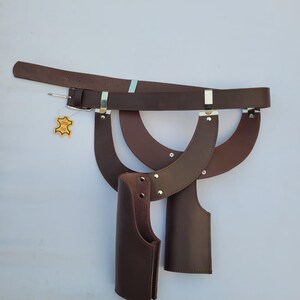 Puede incluir: Un cintur&oacute;n de cuero marr&oacute;n con hebilla y fundas de cuero adjuntas. El cintur&oacute;n tiene detalles met&aacute;licos plateados y una peque&ntilde;a etiqueta. Las fundas est&aacute;n dise&ntilde;adas para guardar objetos y est&aacute;n unidas al cintur&oacute;n.