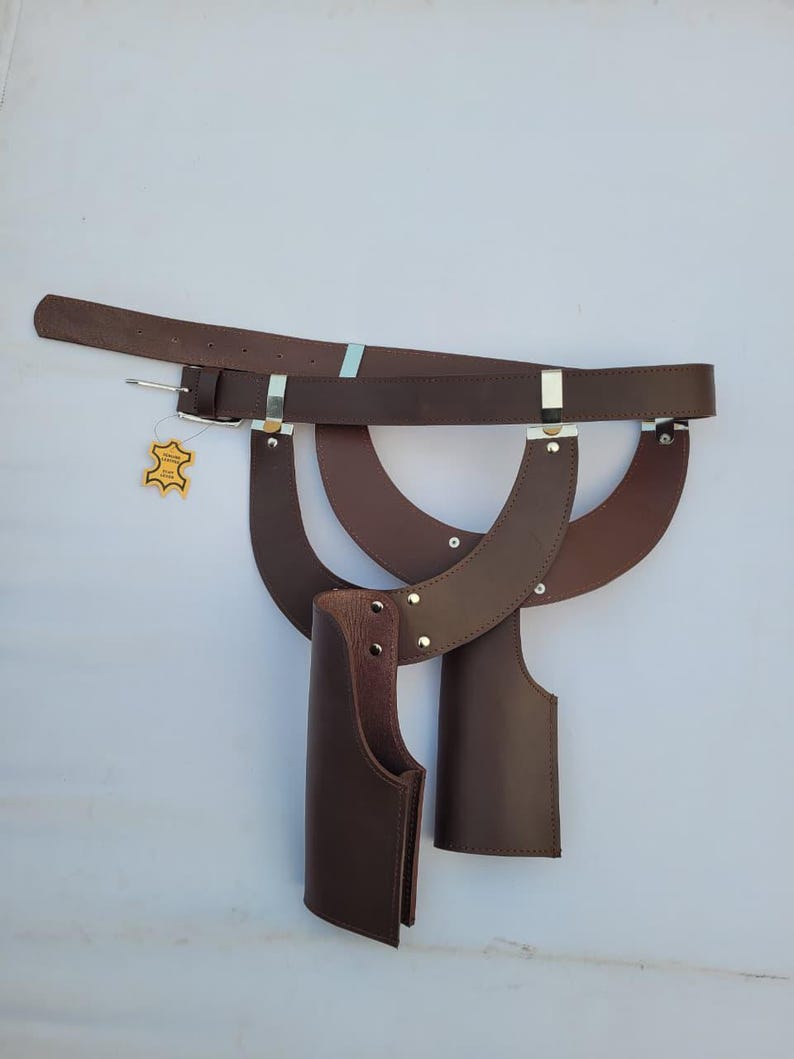 Puede incluir: Un cintur&oacute;n de cuero marr&oacute;n con hebilla y fundas de cuero adjuntas. El cintur&oacute;n tiene detalles met&aacute;licos plateados y una peque&ntilde;a etiqueta. Las fundas est&aacute;n dise&ntilde;adas para guardar objetos y est&aacute;n unidas al cintur&oacute;n.