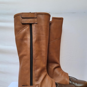 Puede incluir: Un par de botas de montar de cuero marr&oacute;n con una cremallera en el lateral y una correa con hebilla en la parte superior. Las botas est&aacute;n gastadas y tienen un ligero roce en la punta.