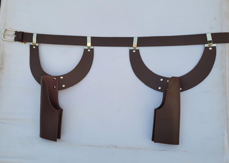 Puede incluir: Un cintur&oacute;n de cuero marr&oacute;n con dos piezas de cuero curvadas adjuntas y dos bolsas de cuero marr&oacute;n. El cintur&oacute;n tiene una hebilla plateada y detalles met&aacute;licos plateados. Las bolsas est&aacute;n unidas a las piezas de cuero curvadas con remaches.