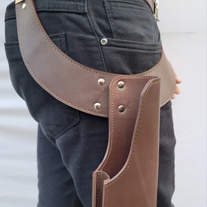 Puede incluir: Cintur&oacute;n de cuero marr&oacute;n con funda. El cintur&oacute;n tiene una hebilla dorada y est&aacute; asegurado con remaches plateados. La funda est&aacute; dise&ntilde;ada para guardar un objeto y est&aacute; sujeta al cintur&oacute;n.