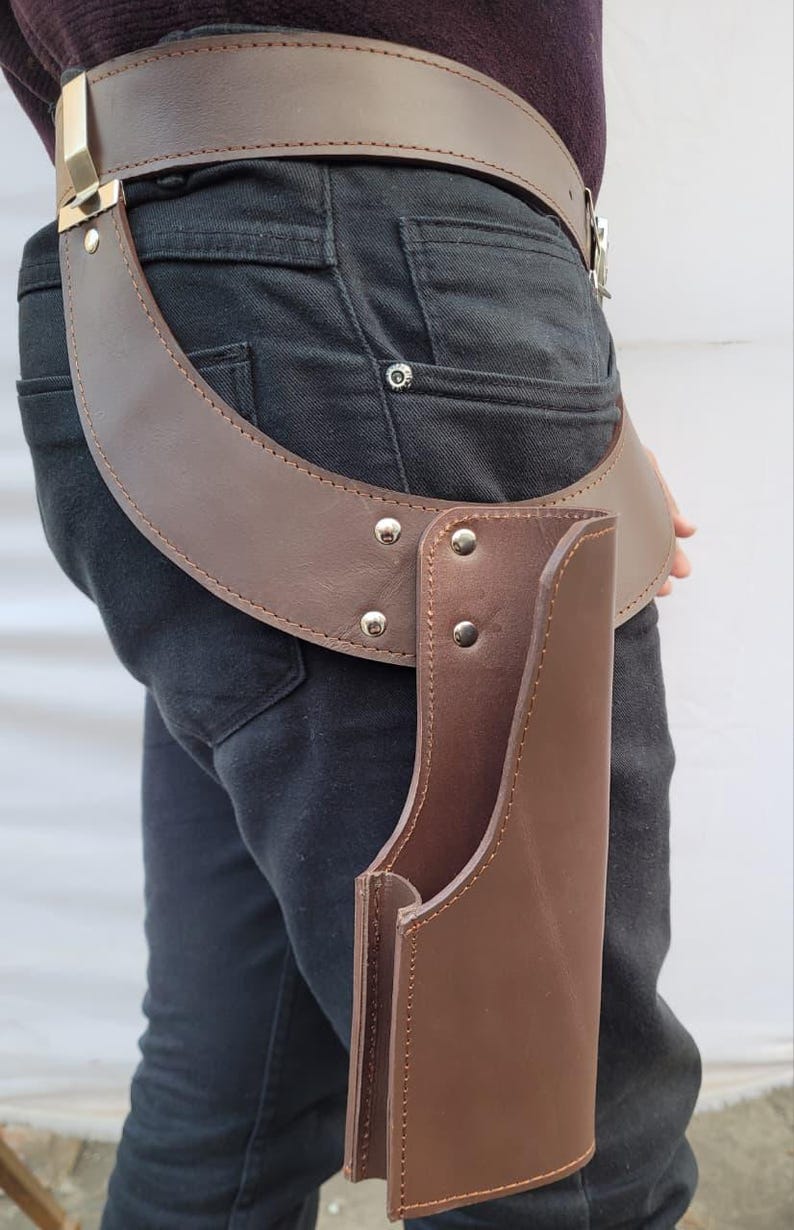 Puede incluir: Cintur&oacute;n de cuero marr&oacute;n con funda. El cintur&oacute;n tiene una hebilla dorada y est&aacute; asegurado con remaches plateados. La funda est&aacute; dise&ntilde;ada para guardar un objeto y est&aacute; sujeta al cintur&oacute;n.