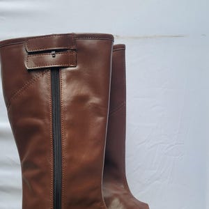 Puede incluir: Un par de botas de montar de cuero marr&oacute;n con una cremallera en el lateral y una correa en la parte superior.