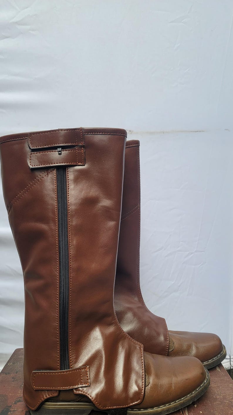 Puede incluir: Un par de botas de montar de cuero marr&oacute;n con una cremallera en el lateral y una correa en la parte superior.