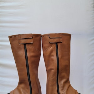 Puede incluir: Un par de botas de montar de cuero marr&oacute;n con cremalleras y hebillas negras. Las botas est&aacute;n hechas de cuero suave y flexible y tienen un ajuste c&oacute;modo.