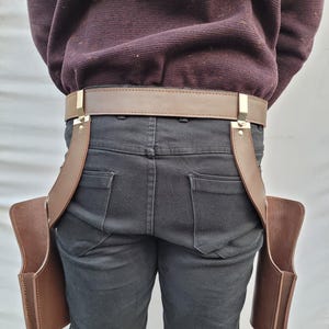 Puede incluir: Un cintur&oacute;n de cuero marr&oacute;n con dos bolsas adjuntas. El cintur&oacute;n tiene una hebilla dorada y se usa con jeans negros. Las bolsas son rectangulares y est&aacute;n dise&ntilde;adas para guardar objetos.