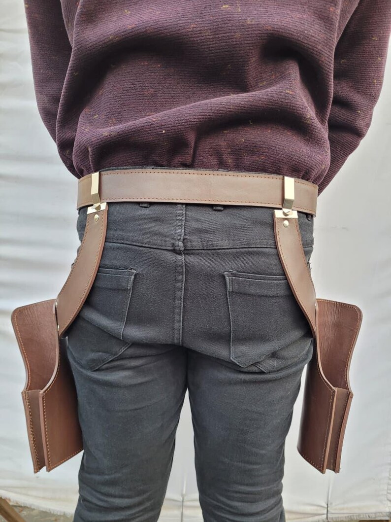 Puede incluir: Un cintur&oacute;n de cuero marr&oacute;n con dos bolsas adjuntas. El cintur&oacute;n tiene una hebilla dorada y se usa con jeans negros. Las bolsas son rectangulares y est&aacute;n dise&ntilde;adas para guardar objetos.