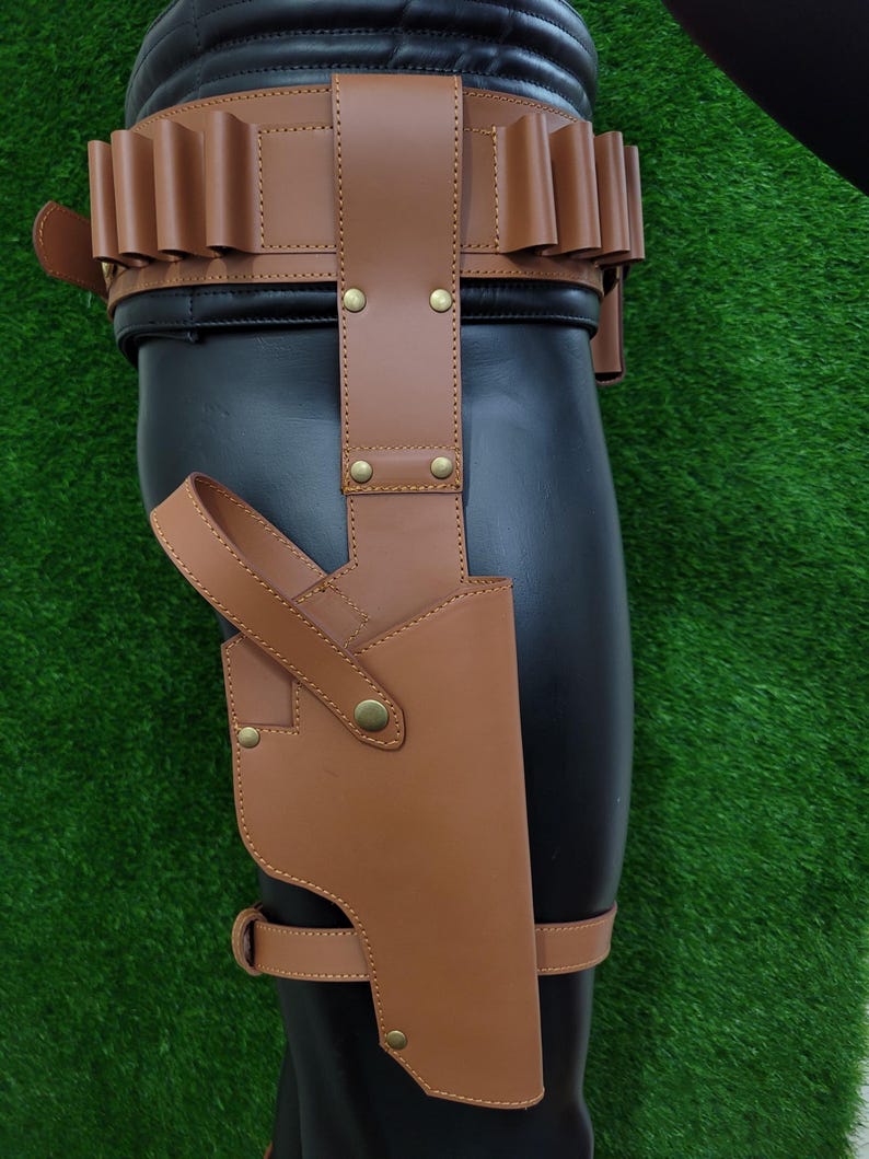 May include: A brown leather holster and belt set. The holster is attached to a leg strap and features a curved design. The belt has multiple loops and is secured with a buckle. The set is made of brown leather and has brass-colored rivets.