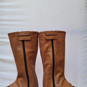 Puede incluir: Un par de botas de montar de cuero marr&oacute;n con cremalleras y hebillas negras. Las botas est&aacute;n hechas de cuero suave y flexible y tienen un ajuste c&oacute;modo.