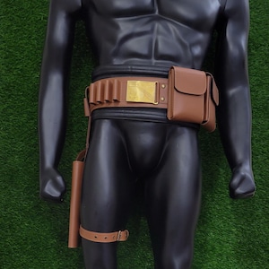 May include: Brown leather utility belt with a gold-colored buckle and a matching holster and pouch. The belt features loops for holding items and a thigh strap. The mannequin is displayed against a green background.