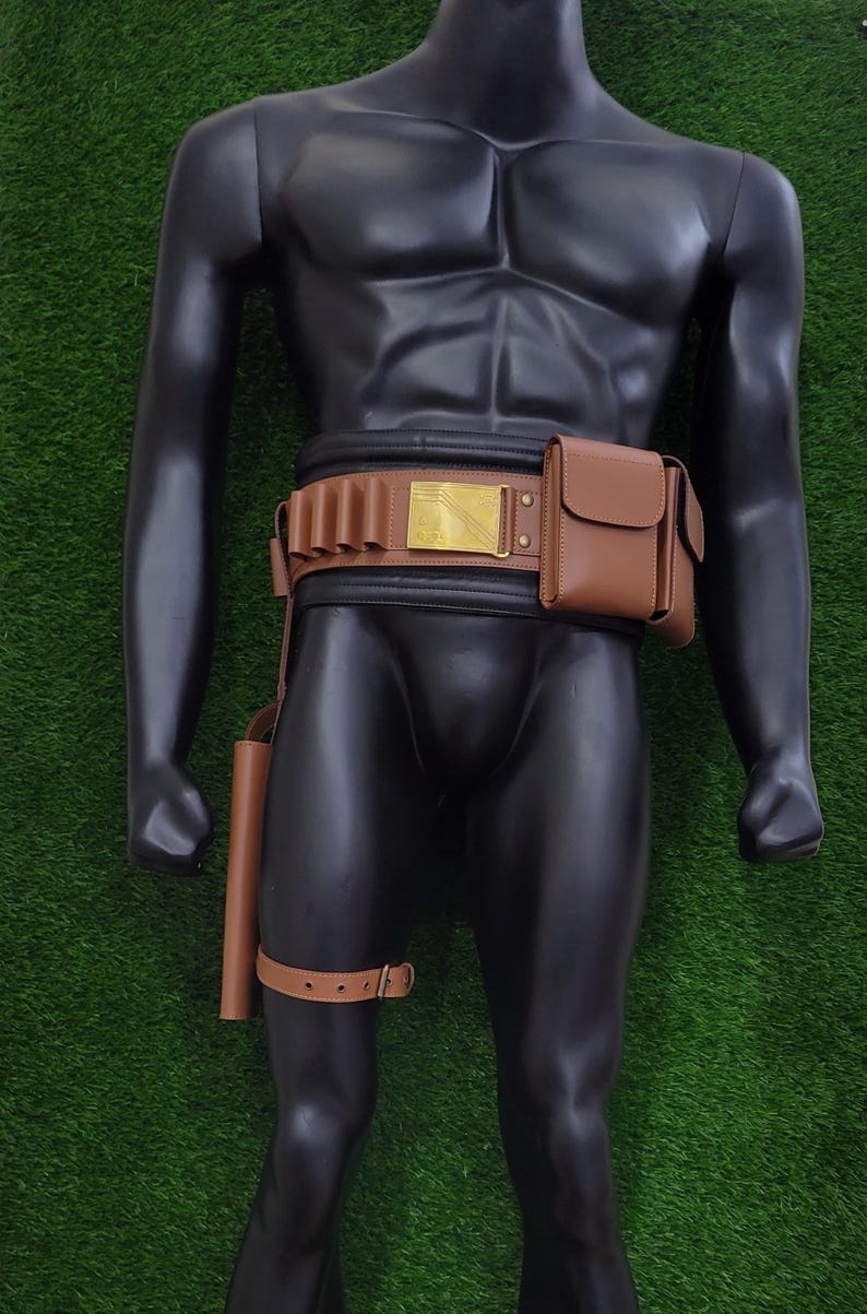 May include: Brown leather utility belt with a gold-colored buckle and a matching holster and pouch. The belt features loops for holding items and a thigh strap. The mannequin is displayed against a green background.