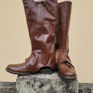 Puede incluir: Un par de botas de cuero marr&oacute;n con ca&ntilde;a alta. Las botas est&aacute;n sobre un bloque de hormig&oacute;n.