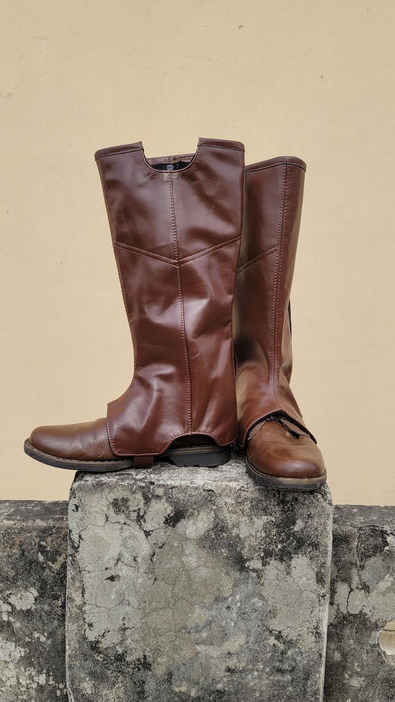 Puede incluir: Un par de botas de cuero marr&oacute;n con ca&ntilde;a alta. Las botas est&aacute;n sobre un bloque de hormig&oacute;n.