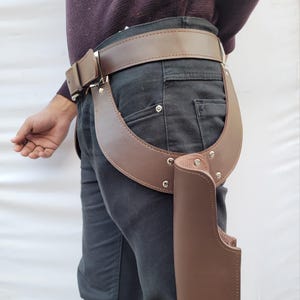 Puede incluir: Juego de cintur&oacute;n y funda de pistola de cuero marr&oacute;n. El cintur&oacute;n es de color marr&oacute;n medio con una hebilla plateada. La funda est&aacute; sujeta al cintur&oacute;n y tiene una pieza de soporte curvada. El conjunto est&aacute; dise&ntilde;ado para llevarse en la cadera.