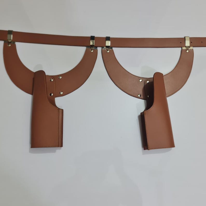 Puede incluir: Un arn&eacute;s de cuero color canela con un cintur&oacute;n horizontal conectado a dos piezas de hombro sim&eacute;tricas en forma de media luna. Cada lado incluye un accesorio de funda vertical asegurado con remaches met&aacute;licos y herrajes dorados.