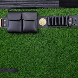 May include: Black leather utility belt with two pouches, cartridge holders, and a gold-colored buckle. The belt features a gold-colored emblem and is set against a green background.