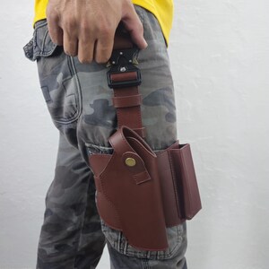 May include: A brown leather holster with a matching magazine pouch attached. The holster is secured to the leg with a brown leather strap and a black metal buckle. The person is wearing camouflage pants and a yellow shirt.