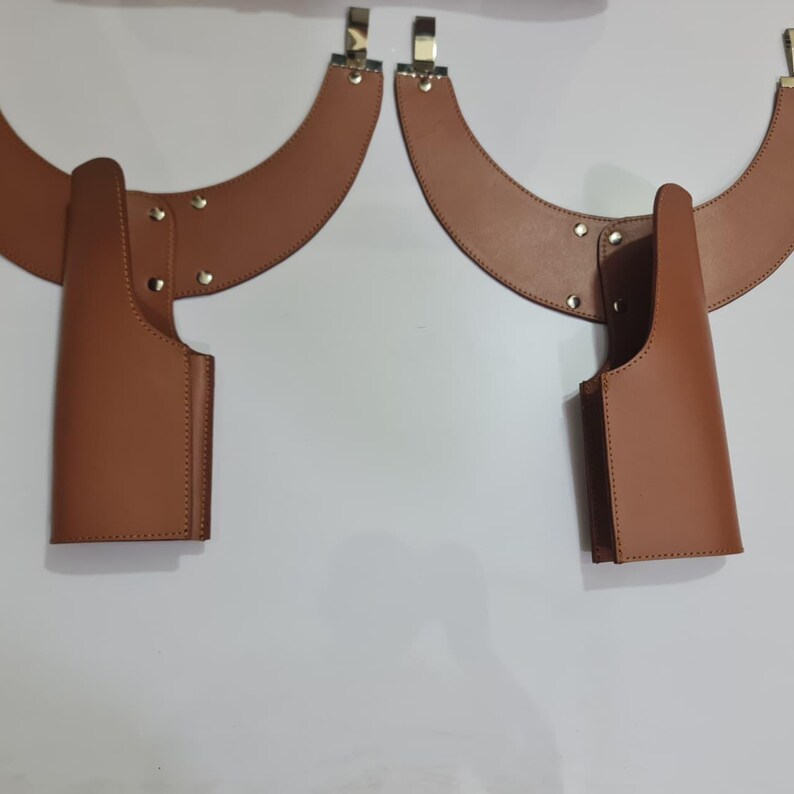 Puede incluir: Dos fundas de hombro de cuero color canela con paneles de yugo curvos y bolsas verticales. Cada funda est&aacute; asegurada con remaches de metal plateado e incluye un clip de metal plateado en el borde superior para su fijaci&oacute;n, con un dise&ntilde;o sim&eacute;trico.