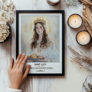 May include: Framed print of Saint Lucy, patron saint of the blind and eye diseases. The artwork depicts a woman with a halo and crown, holding a plate of bread. The print is in a black frame, with text at the bottom.