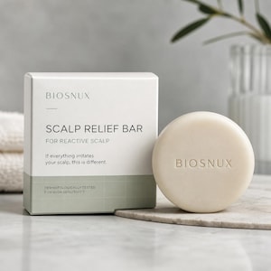 May include: A white rectangular box labeled BIOSNUX SCALP RELIEF BAR FOR REACTIVE SCALP with a light green grid pattern at the base, accompanied by a round, off-white solid soap bar embossed with the brand name BIOSNUX on its front surface.