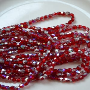 May include: A strand of red iridescent glass beads. The beads are faceted and have a shiny finish.