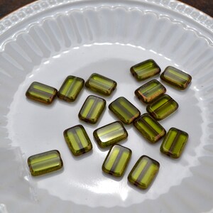 May include: A collection of green glass beads with gold accents. The beads are rectangular in shape and have a glossy finish.