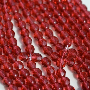 May include: Close-up of strands of faceted, translucent red beads. The beads are strung together, creating rows of sparkling, jewel-toned accents. The beads have a geometric, multi-faceted design, reflecting light.