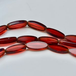 May include: A strand of oval-shaped, translucent red glass beads. The beads have a striated pattern and are strung together on a clear thread.