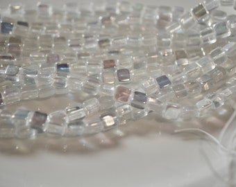 May include: A strand of clear glass beads with iridescent accents. The beads are square shaped and have a slightly irregular shape.