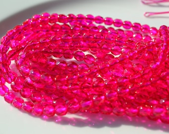 May include: Close-up of a collection of bright pink faceted beads. The beads are strung together, creating multiple strands. The beads are round with multiple facets, reflecting light. The background is white, and the beads are the focal point.