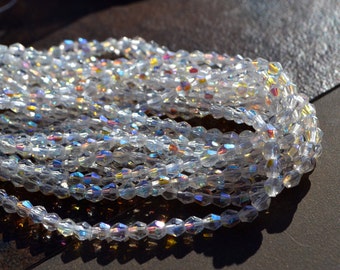 May include: Strands of clear, iridescent beads. The beads are small, faceted, and reflect a rainbow of colors. The beads are strung together, creating a shimmering effect. The beads are likely used for jewelry making or other crafts.