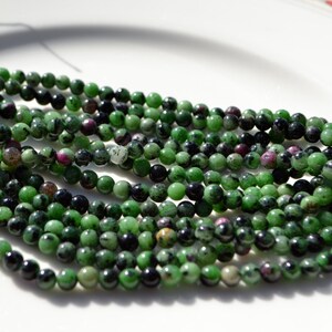 May include: A strand of green, black, and pink gemstone beads. The beads are round and have a smooth, polished finish.