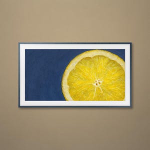 May include: A framed art print showing a close-up of a sliced lemon. The bright yellow citrus fruit is set against a deep blue background. The artwork is framed in a dark blue frame.