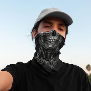 May include: A black and grey face covering featuring a detailed skull design. The skull has a mechanical appearance with gears and tubes. The person is wearing a grey baseball cap and a black shirt.