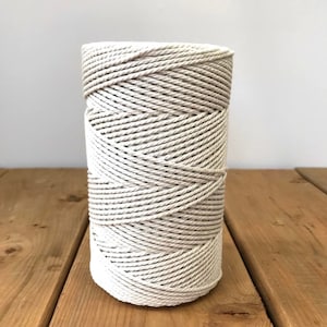 May include: A spool of natural-coloured cotton rope. The rope is tightly wound and has a smooth, slightly textured surface.