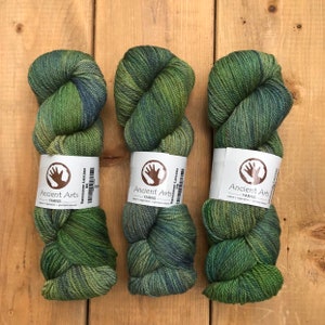 Könnte beinhalten: Drei Knäuel grüner, blauer und gelber Wolle mit einem weißen Etikett, auf dem "Ancient Arts Yarns" und "Vancouver-Lascaux DK" steht.
