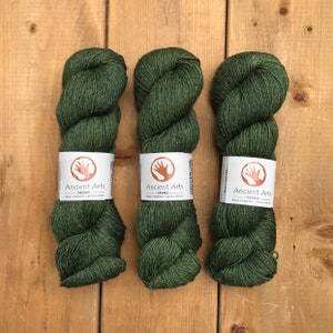 Puede incluir: Tres ovillos de hilo verde oscuro con una etiqueta marrón que dice "Ancient Arts Yarns - Nature, Inspiration, Genuine Colour".