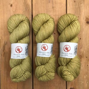 Peut inclure: Trois écheveaux de fil vert étiquetés "Ancient Arts Yarns" avec le texte "Anjou-Floritura Worsted" sur l'étiquette.