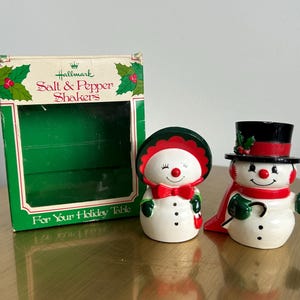 May include: Hallmark salt and pepper shakers in the shape of snowmen. One snowman wears a top hat and cape, the other a bonnet and bow tie. The box reads "For Your Holiday Table."