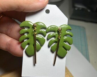 Monstera Polymer Clay Earrings with a golden bar hanging down in the front.