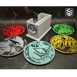 May include: Six colorful coasters featuring Pokemon characters. The coasters are round and made of a 3D printed material. A white holder with a Pokemon logo is in the center of the image.
