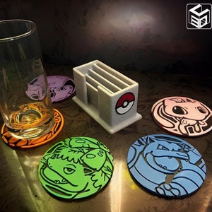 May include: Five colorful round coasters with different Pokemon characters printed on them. The coasters are made of a hard plastic material and are about 4 inches in diameter. There is a gray plastic card holder in the center of the image.