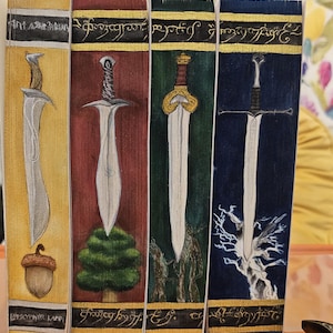 May include: Four illustrated bookmarks featuring swords. Each bookmark has a different background color: yellow, red, green, and blue. The swords are drawn in detail, with varying designs and styles. The bookmarks have text at the top and bottom.