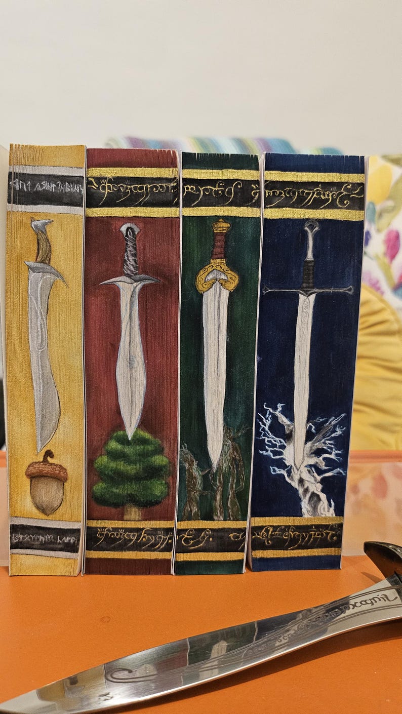 May include: Four illustrated bookmarks featuring swords. Each bookmark has a different background color: yellow, red, green, and blue. The swords are drawn in detail, with varying designs and styles. The bookmarks have text at the top and bottom.
