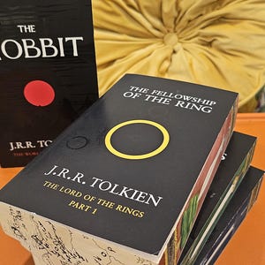 May include: Stack of J.R.R. Tolkien's "The Lord of the Rings" books, with "The Fellowship of the Ring" visible. The book covers are black with gold and yellow accents. "The Hobbit" book is also visible.