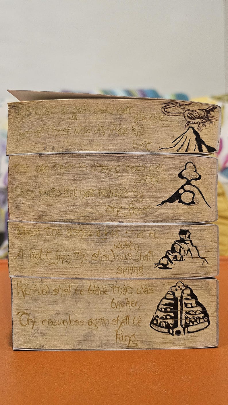 May include: Four wooden blocks with etched text and illustrations. The text includes phrases like "A light from the shadows shall spring" and "The crownless again shall be king." Each block features a different black ink illustration.