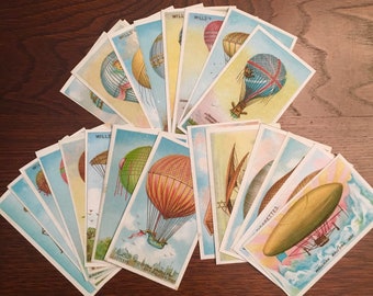 May include: A collection of vintage cigarette cards featuring illustrations of hot air balloons and airships. The cards are printed with the text "Wills's Cigarettes" and feature various designs, including a red, white, and blue balloon, a green and white balloon, and a brown and yellow balloon.