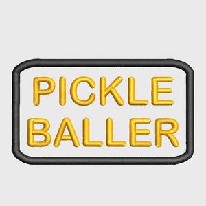 May include: Embroidered patch featuring the text "PICKLE BALLER" in gold thread. The words are within a white rectangle with a black border. Suitable for application on clothing or accessories.